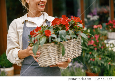 Close up of woman florist business owner standing with houseplants on background of floral store Close up of woman florist business owner standing with houseplants on background of floral store 104560456