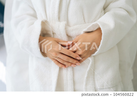 Close-up cropped shot of unrecognizable young woman wearing white bathrobe holding hands by stomach in spa salon after treatment procedures. Concept of luxury professional massage in beauty clinic. 104560822