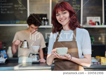 Portrait of young female waitress in front of counter in coffee shop Portrait of young female waitress in front of counter in coffee shop 104561998