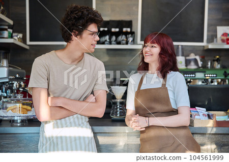 Young coffee shop workers talking, standing in front of counter in cafeteria Young coffee shop workers talking, standing in front of counter in cafeteria 104561999