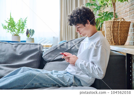 Young guy using smartphone, sitting on sofa in living room 104562038