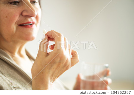 Close up of a retired woman in casual clothes at home holding pill and glass water.  104562297