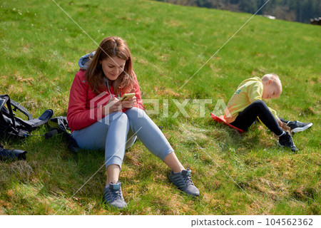 Young tourist girl resting with phone on the top of the mounting landscape. Hiking woman relaxing. Caucasian beautiful woman wearing casual clothes, adventure traveling alone and hiking on the top of 104562362