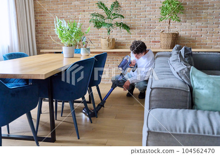 Young guy doing vacuuming, at home in the living room 104562470