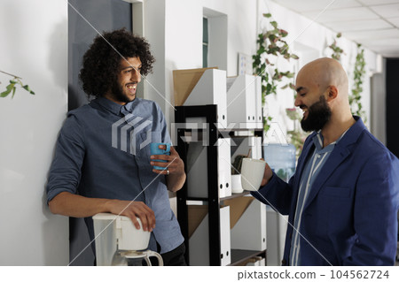 Businessmen enjoying coffee break together and laughing while relaxing in corporate office. Smiling arab young start up company employees mates chatting in coworking space 104562724