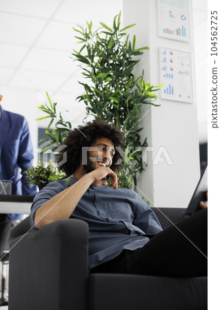 Arab start up entrepreneur laughing while talking in online meeting on digital tablet in office. Smiling business company worker using corporate videocall application to chat with coworkers 104562725
