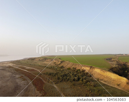 a plowed field and a rugged shore with trees and rural road 104563083