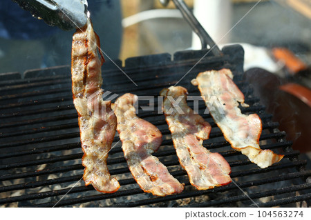 bacon slices roasted on grill bar closeup photo with cooks hands bacon slices roasted on grill bar closeup photo with cooks hands 104563274