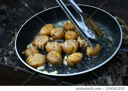 new jacket potatoes roasting in frying pan on grill coals closeup photo 104563291