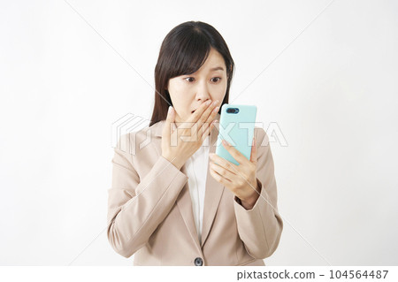 Surprised middle-aged business woman looking at her smartphone White background 104564487
