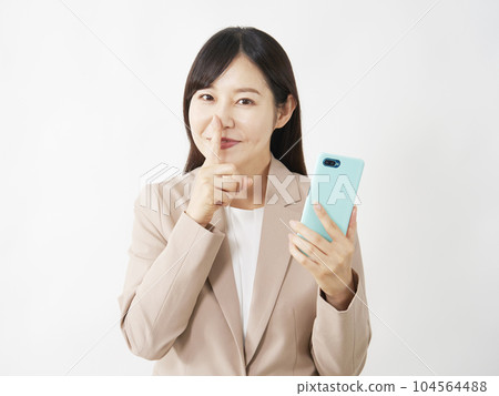 A middle-aged business woman holding a smartphone and posing secretly White background 104564488