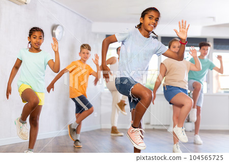 Positive juvenile boy engaged in Hip-hop dance in training room with children's group 104565725