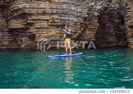 Young men Having Fun Stand Up Paddling in blue water seaamong the rocks in Montenegro. SUP Young men Having Fun Stand Up Paddling in blue water seaamong the rocks in Montenegro. SUP 104569033