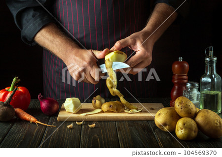 The chef is cleaning potatoes in the kitchen. Hands of a cook with a knife while preparing delicious food. Vegetable diet menu for restaurant or hotel The chef is cleaning potatoes in the kitchen. Hands of a cook with a knife while preparing delicious food. Vegetable diet menu for restaurant or hotel 104569370