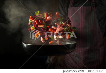 Chef prepares food in a hot pan with steam on a black background. The concept of restaurant and hotel service. Grande cuisine. Chef prepares food in a hot pan with steam on a black background. The concept of restaurant and hotel service. Grande cuisine. 104569435
