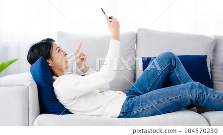 Female smile lying on sofa and holding mobile smartphone Female smile lying on sofa and holding mobile smartphone 104570230