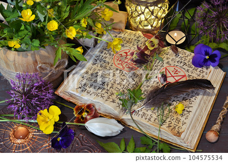 Still life with magic book of spells, candles and flowers on witch table. Occult, esoteric and witchcraft concept. Mystic background with vintage objects Still life with magic book of spells, candles and flowers on witch table. Occult, esoteric and witchcraft concept. Mystic background with vintage objects 104575534