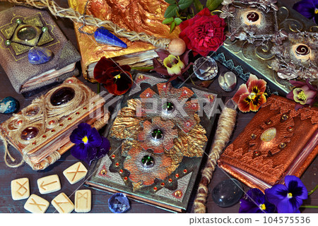 Still life with magic book of spells and fairy tales, runes and flowers on the table. Occult, esoteric and witchcraft concept. Mystic background with vintage objects Still life with magic book of spells and fairy tales, runes and flowers on the table. Occult, esoteric and witchcraft concept. Mystic background with vintage objects 104575536