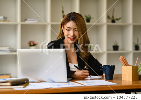 Beautiful woman entrepreneur watching online webinar on laptop and making importance notes Beautiful woman entrepreneur watching online webinar on laptop and making importance notes 104577223