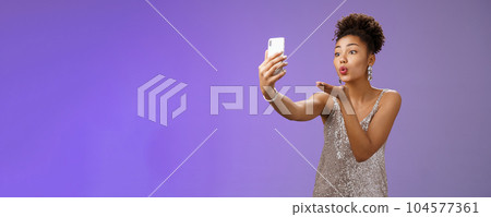 Charming elegant young female student partying enjoying prom recording video smartphone look phone display send air kiss blowing mwah taking selfie hold gadget, standing blue background Charming elegant young female student partying enjoying prom recording video smartphone look phone display send air kiss blowing mwah taking selfie hold gadget, standing blue background 104577361