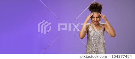 Pressured intense worried african-american woman in silver glittering dress grimacing cringing painful headache hold hand forehead suffer pain migraine, standing bothered blue background Pressured intense worried african-american woman in silver glittering dress grimacing cringing painful headache hold hand forehead suffer pain migraine, standing bothered blue background 104577494