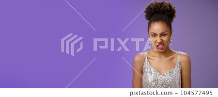 Displeased arrogant african-american woman in silver glittering dress cringing dislike awful smell standing bothered displeased look disgusted frowning standing reluctant blue background Displeased arrogant african-american woman in silver glittering dress cringing dislike awful smell standing bothered displeased look disgusted frowning standing reluctant blue background 104577495