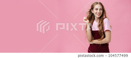 Girl looking like start from glamour magazines posing over pink background feminine and sensual looking right with flirty smile playing with hair while strands flicking in air Girl looking like start from glamour magazines posing over pink background feminine and sensual looking right with flirty smile playing with hair while strands flicking in air 104577499