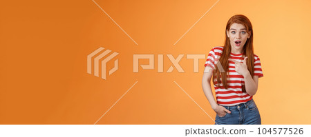 Outgoing good-looking redhead modern girl wonder making amazing purchase, look camera surprised, questioned pointing left, interested about new cool promo, stand orange background Outgoing good-looking redhead modern girl wonder making amazing purchase, look camera surprised, questioned pointing left, interested about new cool promo, stand orange background 104577526