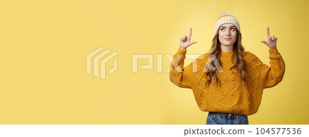 Attractive dreamy stylish college girl wearing hat warm sweater looking up pointing top smiling delighted find curious cool promo recommend you try offer, advertising copy space yellow background 104577536