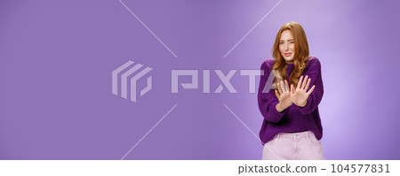 Gross take it away. Portrait of disgusted redhead woman step back and waving palms over body in refusal and no gesture grimacing and squinting from bad smell or aversion over purple wall 104577831