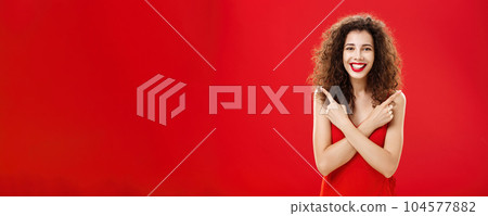 Woman satisfied with any decision feeling carefree and happy standing in elegant red evening dress with curly hairstyle crossing hands on chest pointing left and right delighted with choices Woman satisfied with any decision feeling carefree and happy standing in elegant red evening dress with curly hairstyle crossing hands on chest pointing left and right delighted with choices 104577882