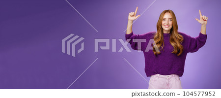 Scroll up and see cool copy space. Portrait of happy attractive and friendly young ginger woman with freckles in warm purple sweater raising hands pointing upwards as showing place Scroll up and see cool copy space. Portrait of happy attractive and friendly young ginger woman with freckles in warm purple sweater raising hands pointing upwards as showing place 104577952
