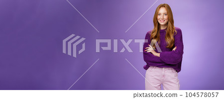 Portrait of pretty young and happy 20s ginger girl in purple sweater holding hands crossed over body smiling broadly, feeling self-assured as promoting project with confidence over violet wall Portrait of pretty young and happy 20s ginger girl in purple sweater holding hands crossed over body smiling broadly, feeling self-assured as promoting project with confidence over violet wall 104578057