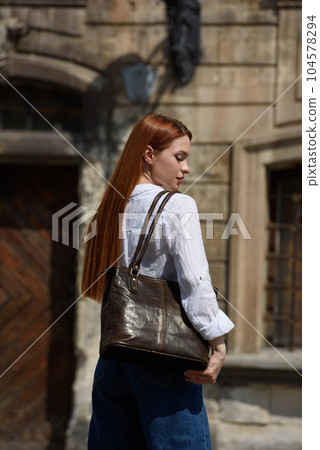 photo of a woman wearing blue jeans and white blouse with a brown leather handbag . photo of a woman wearing blue jeans and white blouse with a brown leather handbag . 104578294