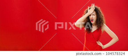 Woman being pissed with dumb people. Irritated forgetful adult caucasian female with curly hair in red elegant dress punching forehead with palm closing eyes and swearing recalling important thing 104578324