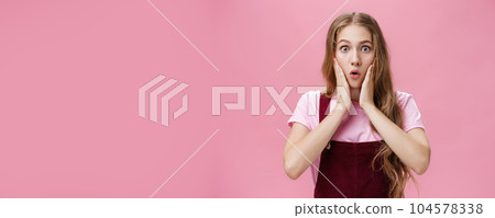 Cute feminine teenage girl in trendy overalls with tattoo on arm folding lips in wow, touching cheeks from amazement and surprise staring at camear shocked and astonished from awesome sales 104578338