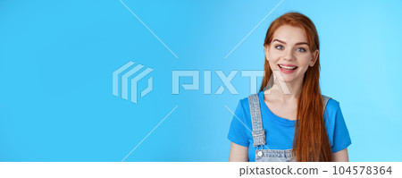 Friendly confident pleasant redhead woman helpfully look camera, smiling joyfully, have conversation customer, give advice, stand upbeat good positive mood blue background, grin amused 104578364