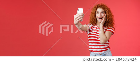Fashionable cute redhead curly female summer t-shirt record video social media from luxury tropical resolt travel holidays abroad take selfie hold smartphone pose silly photograph red background 104578424