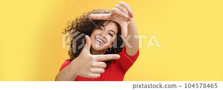 Portrait of optimistic happy and creative female student imaging her new apartment as extending hands and showing frames gesture smiling through it at camera amused and carefree over yellow wall 104578465