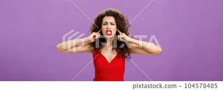 Woman fed up of hearing cursing words and arguments in her turn. Portrait of displeased insecure and offended female with curly hairstyle in red dress closing eyes and talking displeased and bothered Woman fed up of hearing cursing words and arguments in her turn. Portrait of displeased insecure and offended female with curly hairstyle in red dress closing eyes and talking displeased and bothered 104578485