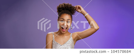 Close-up excited good-looking african-american curly-haired woman in trendy silver glittering dress touching afro curly smiling gladly having fun dancing amused standing entertained blue background Close-up excited good-looking african-american curly-haired woman in trendy silver glittering dress touching afro curly smiling gladly having fun dancing amused standing entertained blue background 104578684