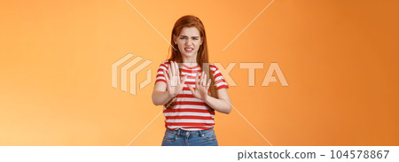 Gosh it stinks. Disgusted redhead picky woman blocking sign raise hands up defensive, grimacing, cringe from aversion awful smell, show refusal rejecting disgusting offer, stand orange background 104578867