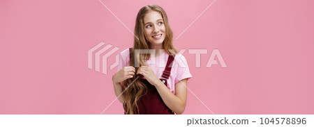 Silly kind and friendly-looking charming girl daydreaming picking strands of hair and looking left with nice cute smile imaging, picturing lovely scene posing flirty and happy over pink background Silly kind and friendly-looking charming girl daydreaming picking strands of hair and looking left with nice cute smile imaging, picturing lovely scene posing flirty and happy over pink background 104578896