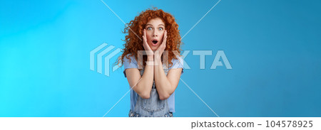Amazed gasping shocked wondered redhead attractive curly girl popping eyes stare camera drop jaw concerned astonished touch cheeks empathy amazement standing blue background Amazed gasping shocked wondered redhead attractive curly girl popping eyes stare camera drop jaw concerned astonished touch cheeks empathy amazement standing blue background 104578925
