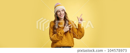 Curious attractive young 20s woman intrigued what hiding left pointing sideways looking interested smiling excited peeking cool fantastic promotion, standing joyfully yellow background 104578973