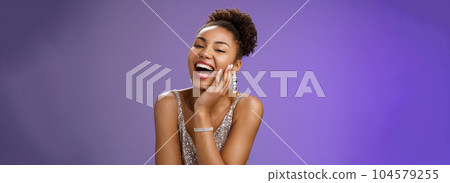 Cheerful attractive happy african american woman in elegant silver light dress laughing flirty giggling enjoying boyfriend sense humour jokes touch cheek coquettish gaze amused, blue background 104579255