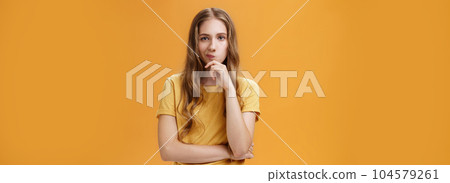 Hmm choices difficult. Portrait of focus serious-looking creative young female with wavy hair smirking holding hand on chin in thoughtful pose, making up decision, thinking over orange background Hmm choices difficult. Portrait of focus serious-looking creative young female with wavy hair smirking holding hand on chin in thoughtful pose, making up decision, thinking over orange background 104579261