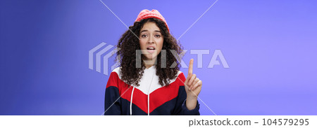 Rule number one do not mess with me babe. Portrait of swag and cool stylish young curly-haired woman in winter beanie showing index finger in prohibition or warning gesture over blue background Rule number one do not mess with me babe. Portrait of swag and cool stylish young curly-haired woman in winter beanie showing index finger in prohibition or warning gesture over blue background 104579295