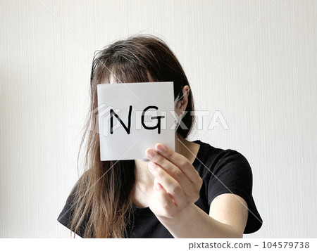 一位女士手拿一張寫有“NG”字樣的紙條在她的面前 一位女士手拿一張寫有“NG”字樣的紙條在她的面前 104579738