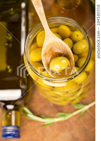 Close up green olives in wooden spoon, rosemary on a wooden background 104580358